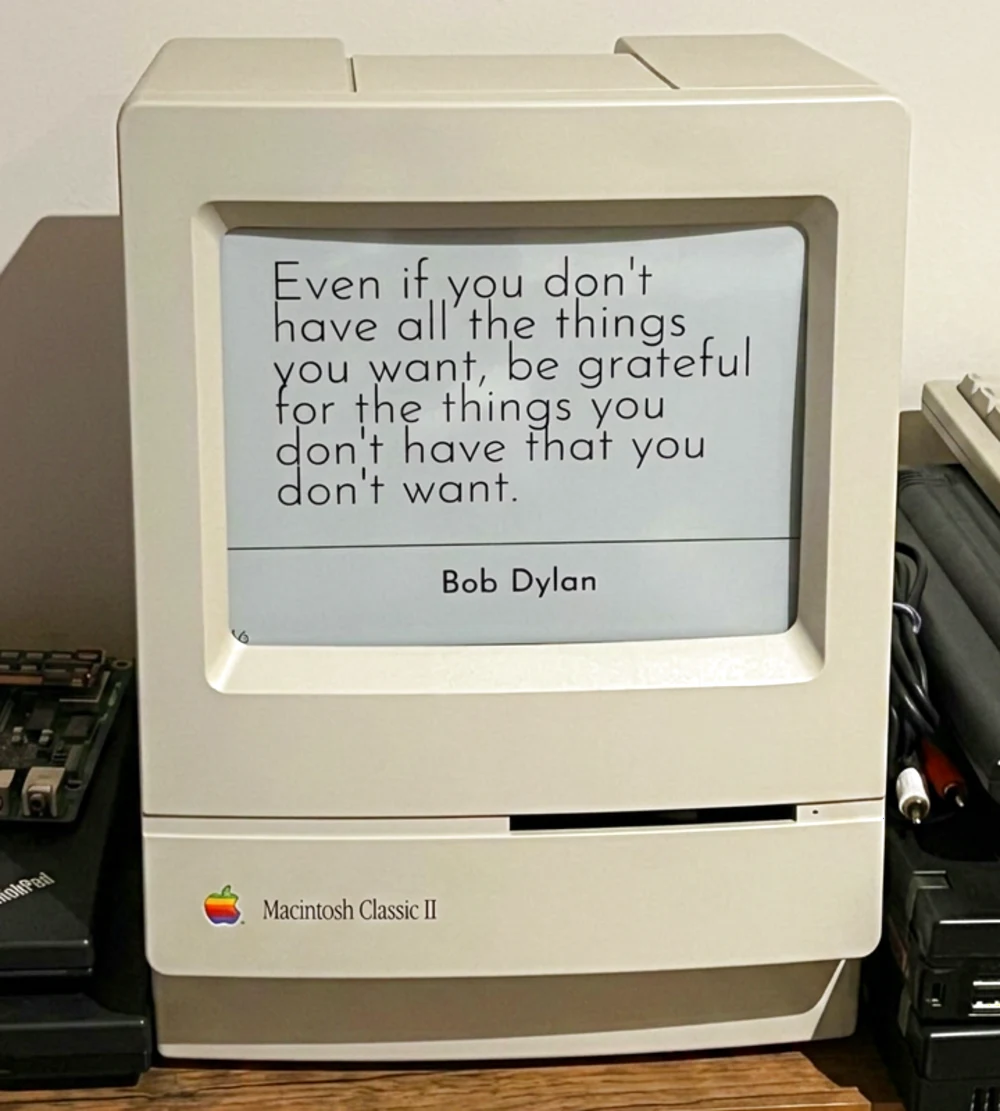 A Macintosh Classic II repurposed as an e-ink display, showing the quote: Even if you don't have all the things you want, be grateful for the things you don't have that you don't want. — Bob Dylan